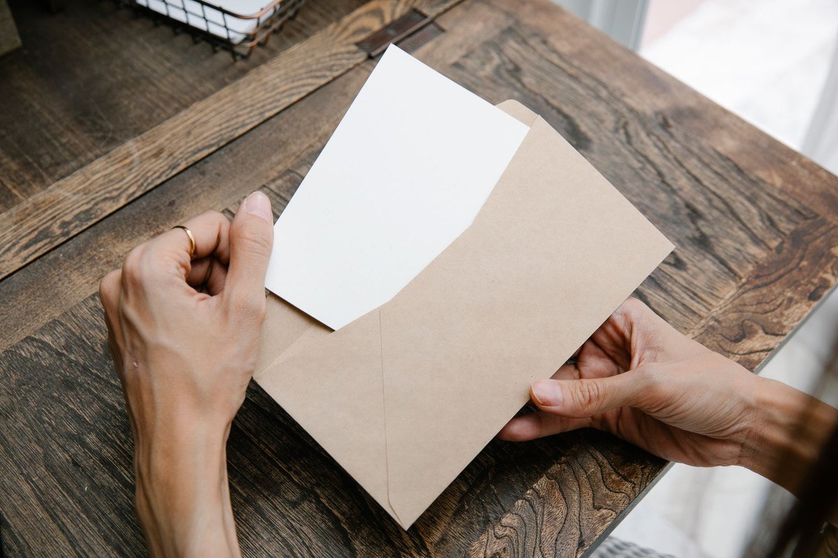 Unas manos sacan una carta de un sobre sobre una mesa de madera