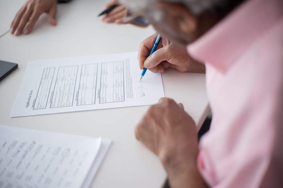 Una persona firma un impreso de solicitud sobre una mesa