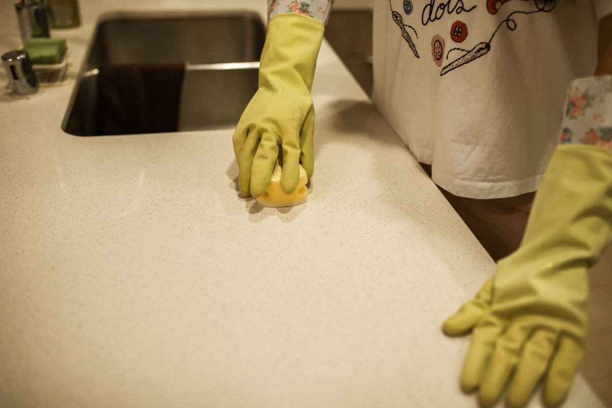 Una empleada de hogar con guantes de goma limpia la encimera de una cocina